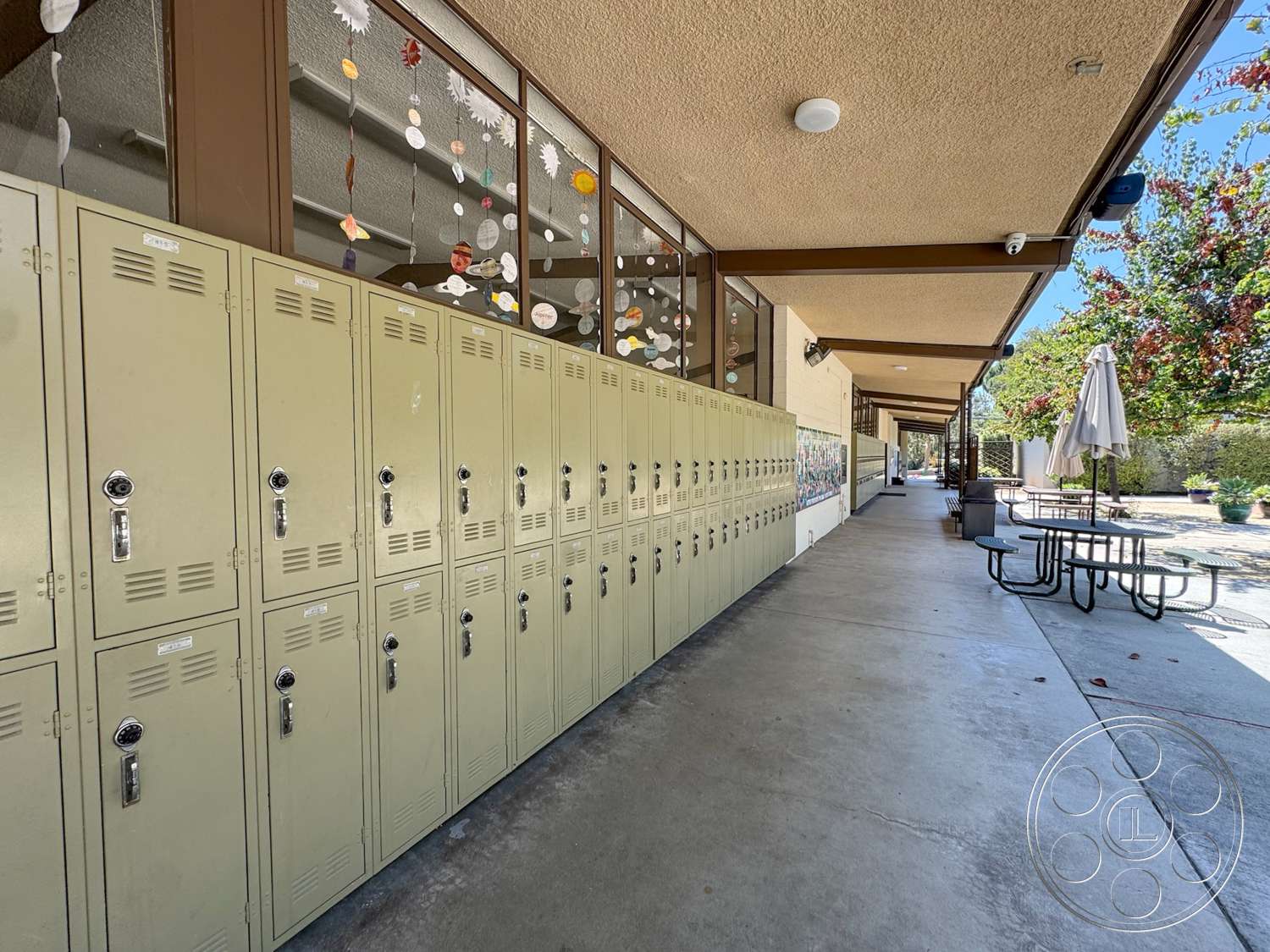 School 20 - exterior, textured plaster ceiling, concrete walkway, metal lockers, landscaped garden area, open courtyard setting, exposed steel support beams, aluminum picnic tables, glass windows with decorative hangings, umbrella patio seating, school building