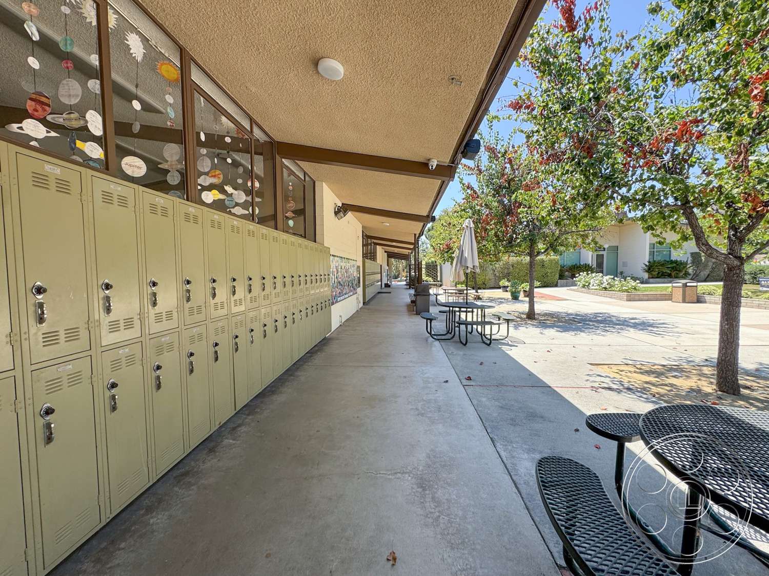 School 20 - exterior, glass windows, decorative wall art, umbrella shading, concrete sidewalk, metal lockers, landscaped garden area, stucco wall finish, aluminum window frames, green metal lockers, overhead awning, outdoor picnic tables, metal table and chair set, growing trees