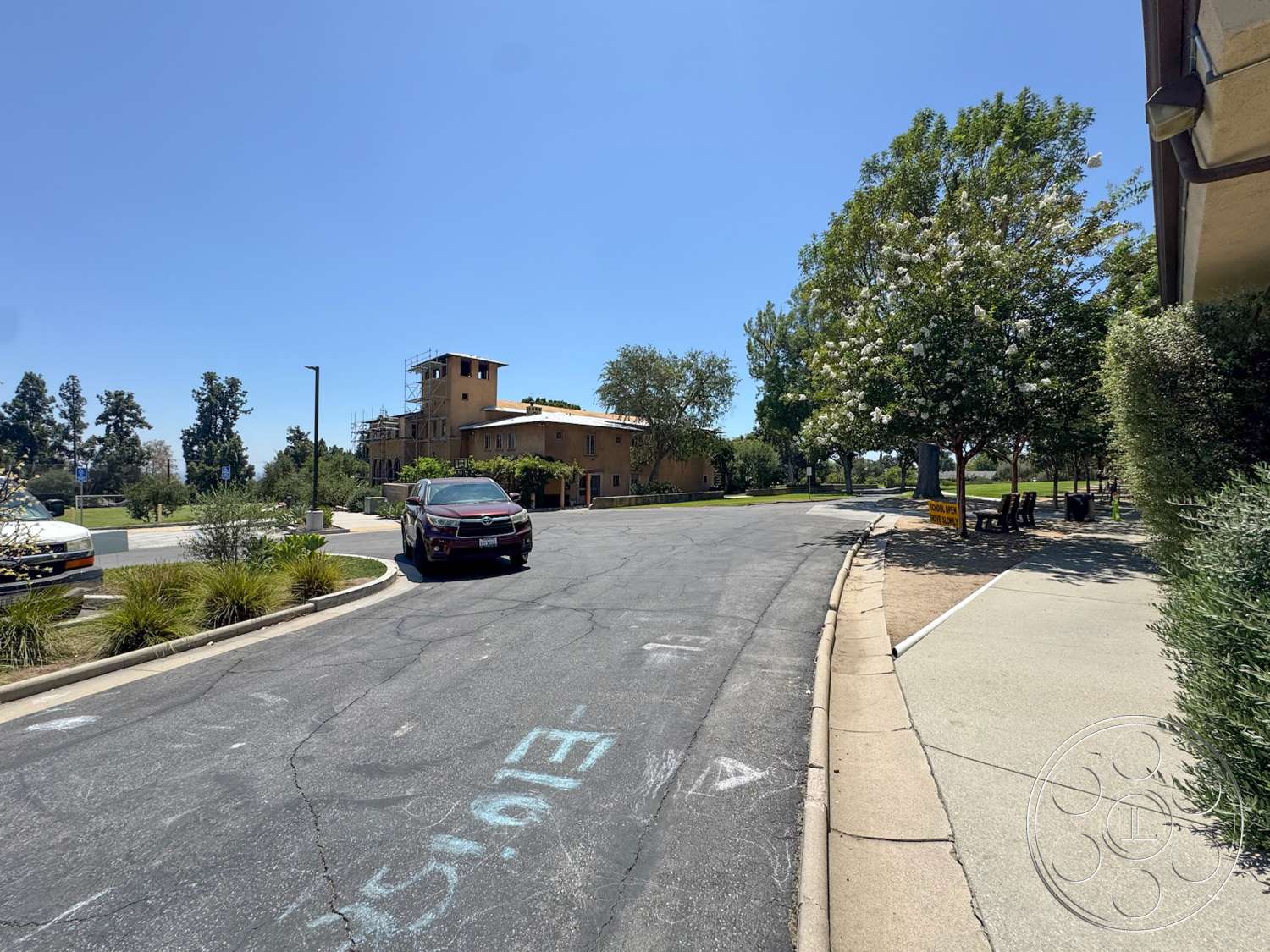 School 20 - flat roof, outdoor seating area, surrounding trees, urban environment, two-story building, asphalt road, concrete sidewalk, stucco exterior walls, wooden balcony railing, landscaped park area