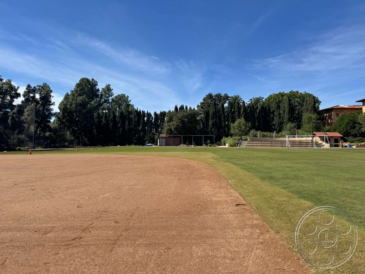 School 20 - exterior, surrounding trees, paved walkway, vibrant greenery, blue sky, park-like setting, outdoor sports facility, open grassy area, natural grass field, dirt baseball infield, sports bleachers
