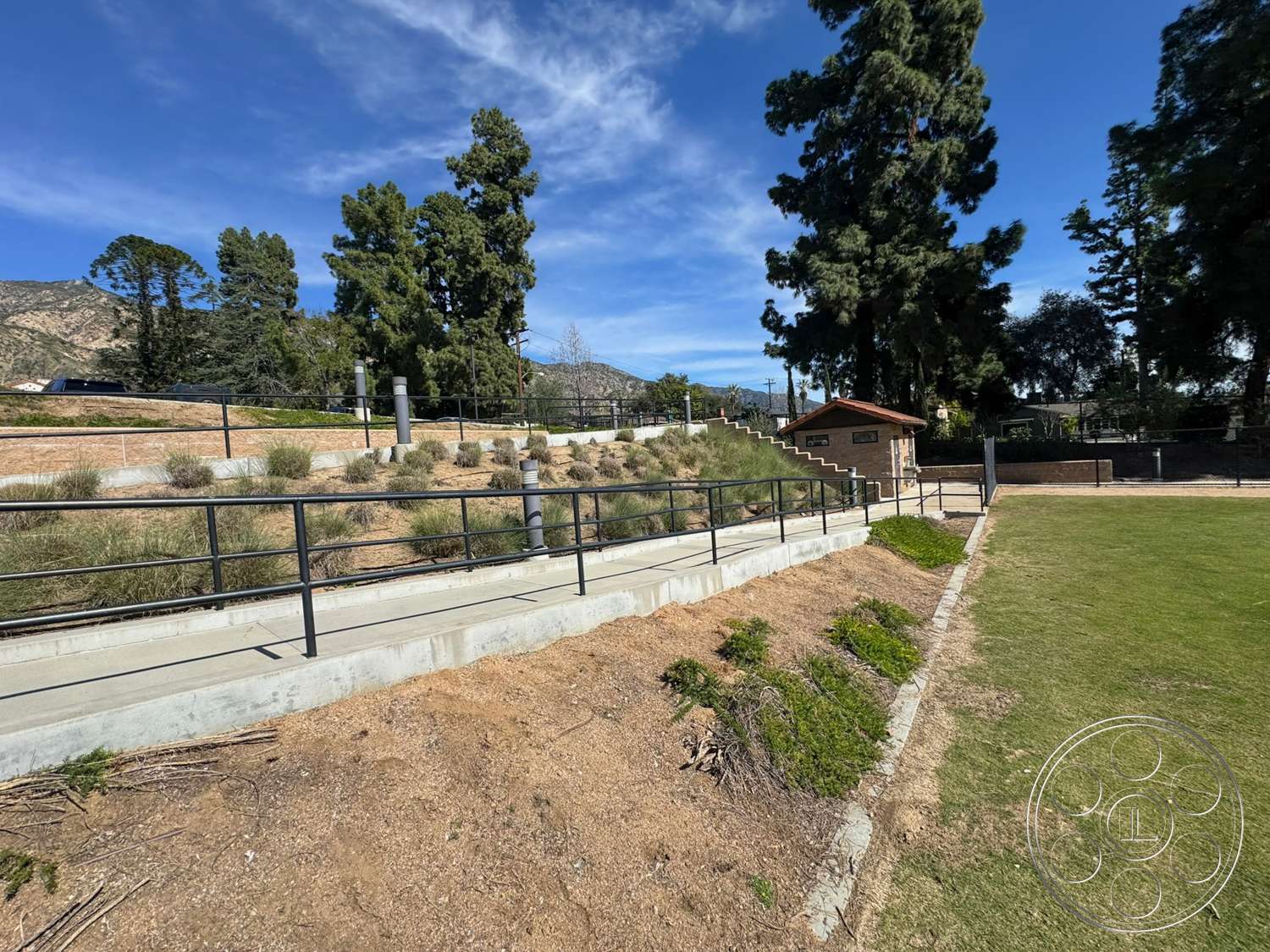 School 20 - outdoor space, metal railing, grass lawn, landscaped hillside, concrete walkway, mountain backdrop, stone retaining wall, residential neighborhood setting, rubberized mulch ground cover, exterior park structure