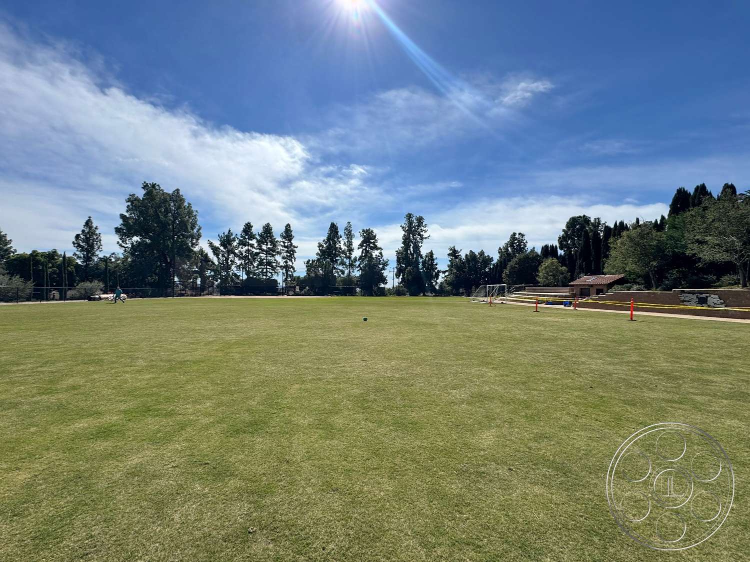 School 20 - exterior, patio area, sunlight, blue sky, tall evergreen trees, manicured grass lawn, soccer goal, landscape lighting posts