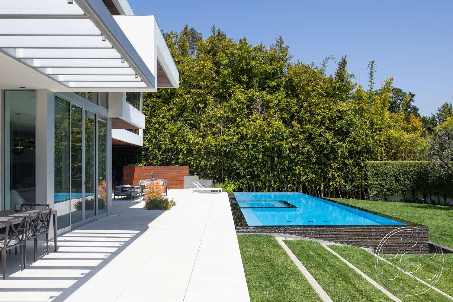 Modern 14 - exterior, glass sliding doors, modern architectural style, clear blue sky, concrete patio flooring, rectangular infinity pool, landscaped garden with bamboo, wood deck furniture, slatted wood privacy screen, horizontal wood overhang