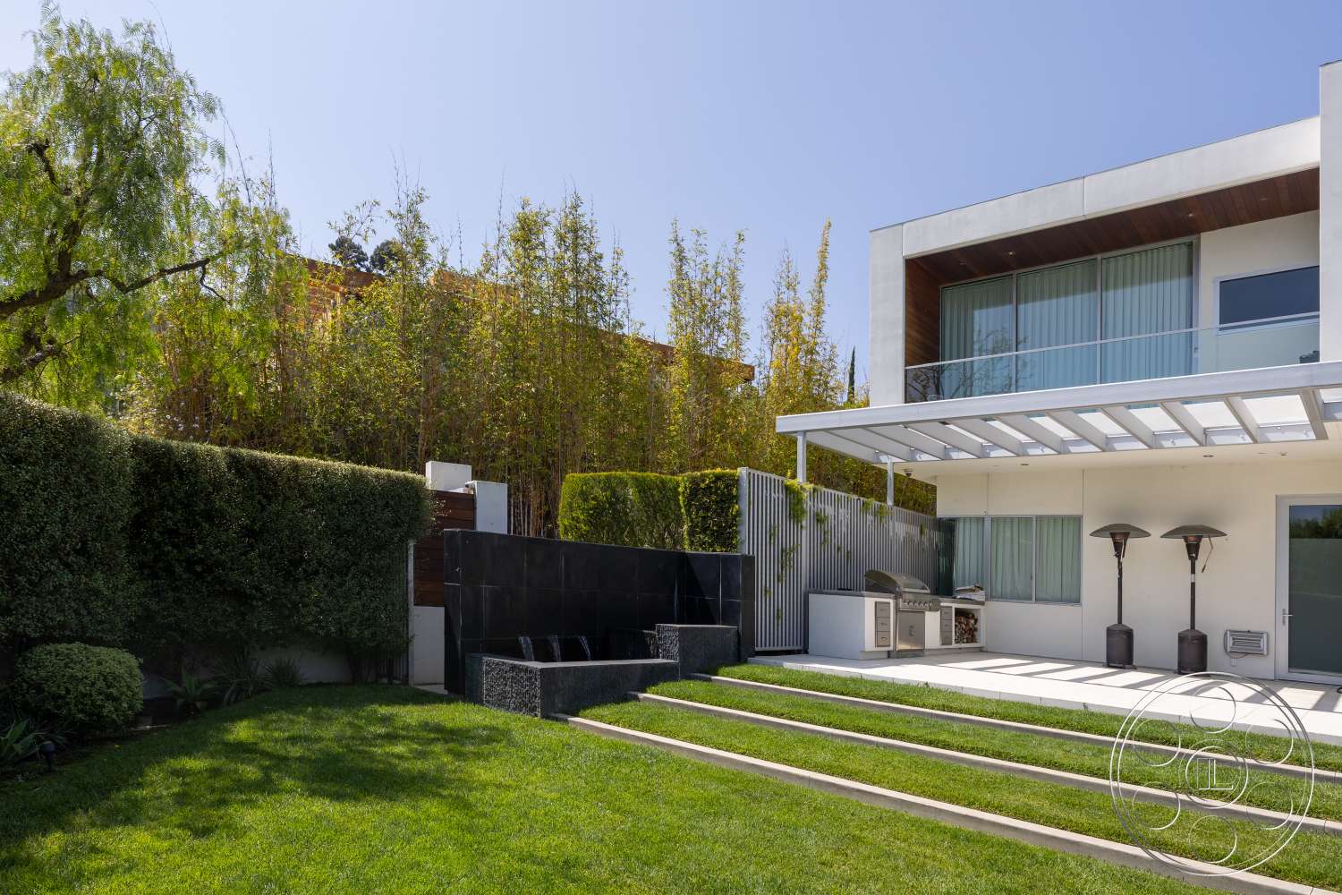 Modern 14 - exterior, modern architecture, glass sliding doors, exposed concrete wall, lawn area, decorative stone wall, concrete patio flooring, horizontal wood fence, rectangular steps, wood beam overhang, outdoor kitchen space, patio heating lamps, green bamboo landscaping