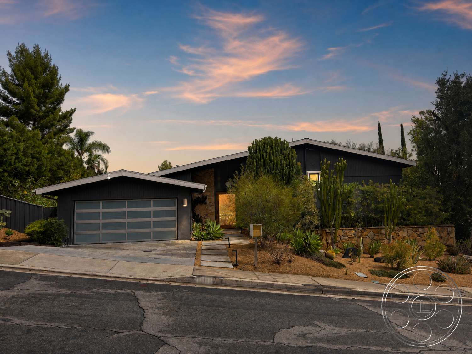 Americana 435 - exterior, flat roof, stone accent wall, sloped terrain, urban setting, floor-to-ceiling windows, landscaped front yard, concrete driveway, attached garage, mid-century modern home, wood siding facade, smooth concrete walkways, gravel garden beds, succulent garden features, sunset sky background
