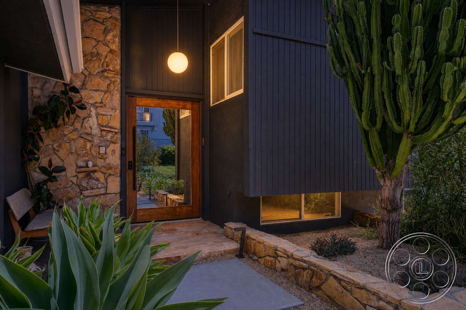 Americana 435 - exterior, concrete pathway, modern architectural style, desert landscaping, succulent plants, wooden front door, vertical wood siding, soft outdoor lighting, stone border wall, natural stone entry wall, large cactus