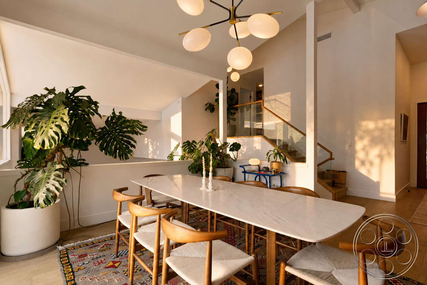 Americana 435 - textured area rug, open floor plan, bright natural light, rectangular dining table, modern light fixture, marble dining table, exposed wood ceiling beams, white painted walls, potted indoor plants, hardwood dining room floors, staircase with wooden railing, mid-century modern dining chairs, comfortable dining space