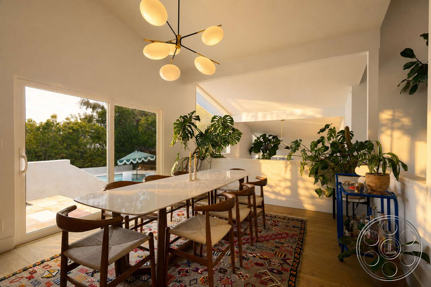 Americana 435 - natural light, contemporary design, wood dining table, glass sliding doors, green indoor plants, open-concept layout, poolside view, wooden dining chairs, white painted walls, wool area rug, minimalist chandelier