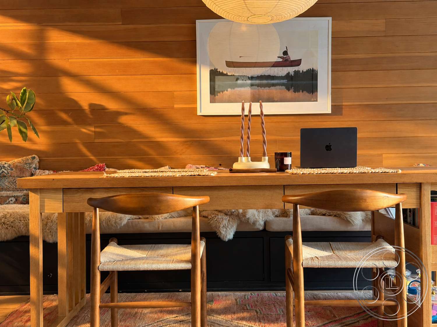 Americana 435 - textured area rug, framed artwork, decorative candles, oak dining table, wood paneling walls, plant accent, upholstered bench seating, woven seat dining chairs, natural fiber table runner, round paper lantern pendant light, windows with natural light, black console storage