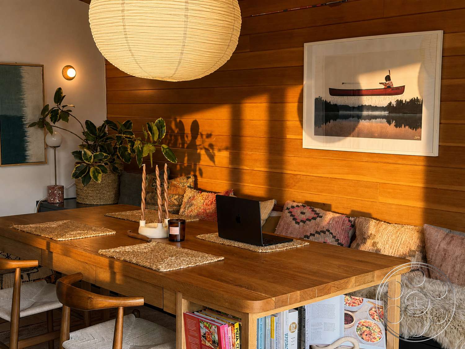 Americana 435 - upholstered dining chairs, light wood dining table, wooden shelves, natural fiber rug, textured fabric cushions, cozy dining nook, indoor potted plants, wood paneling walls, woven placemats, hanging paper lantern light fixture, framed wall art with nature theme