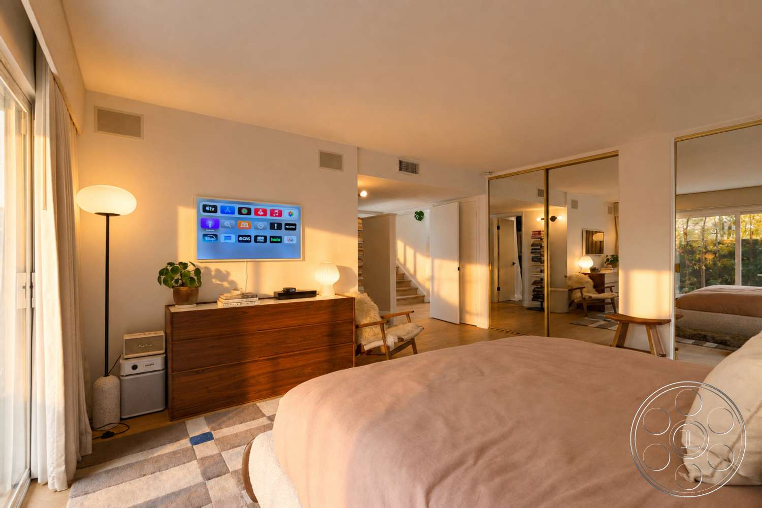 Americana 435 - hardwood flooring, contemporary decor, indoor plant, wooden dresser, floor-to-ceiling windows, textured plaster walls, mirrored closet doors, mid-century modern lamp, square rug with geometric pattern, modern LED television, pleated curtain drapes, overstuffed fabric chair, open-plan bedroom