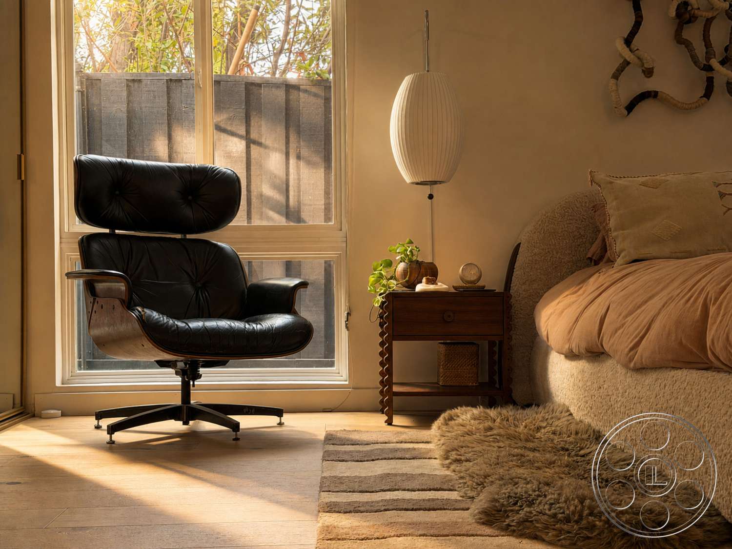 Americana 435 - natural light, light hardwood flooring, large glass windows, textured wall finish, decorative bedside lamp, woven area rug, soft textile cushions, earth-toned color palette, cozy bedding, minimalist bedside table, black leather lounge chair, wooden chair base, plant on bedside table, sculptural wall decor