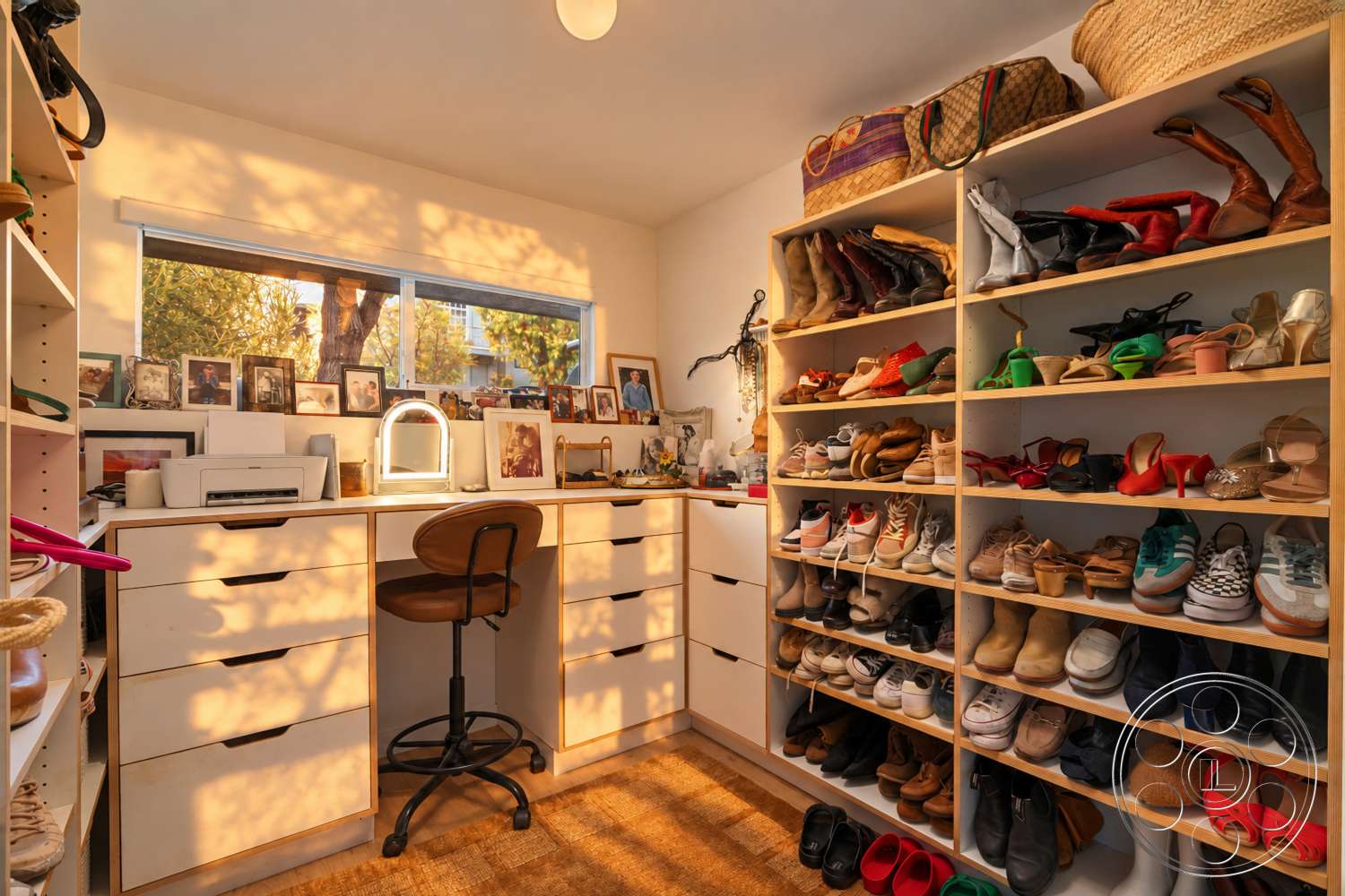 Americana 435 - ambient lighting fixture, eclectic decor elements, large window with natural light, white painted walls, wood laminate flooring, decorative photo frames, built-in shoe shelves, modern desk with drawer storage, round upholstered stool, organized shoe collection, open storage shelving