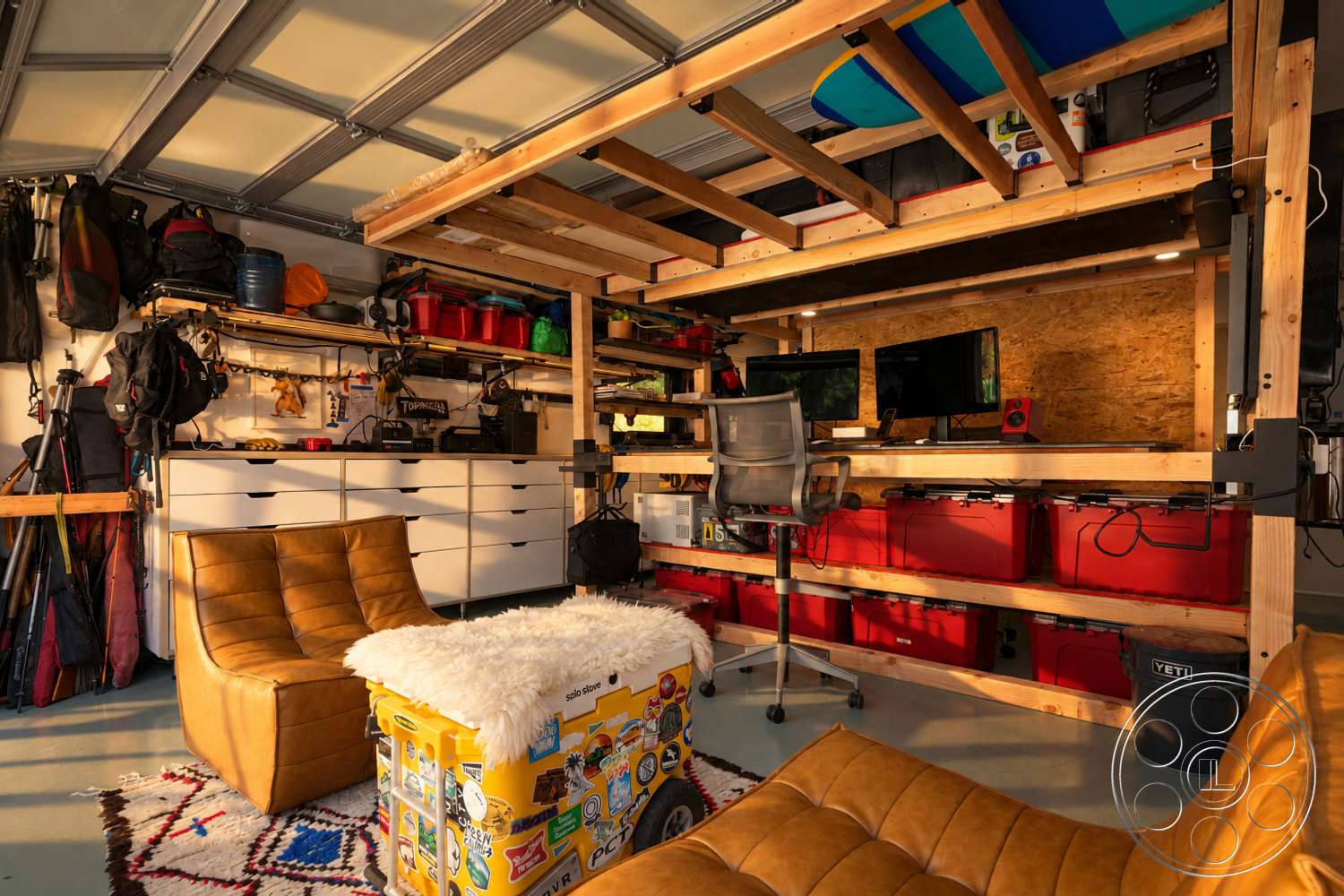Americana 435 - wooden shelving units, exposed wood ceiling beams, stacked storage bins, polished concrete garage floor, metal office chair, textured fabric throw, fabric accent chair, low-pile area rug, OSB plywood wall panels, two-monitor workstation, functional garage workspace