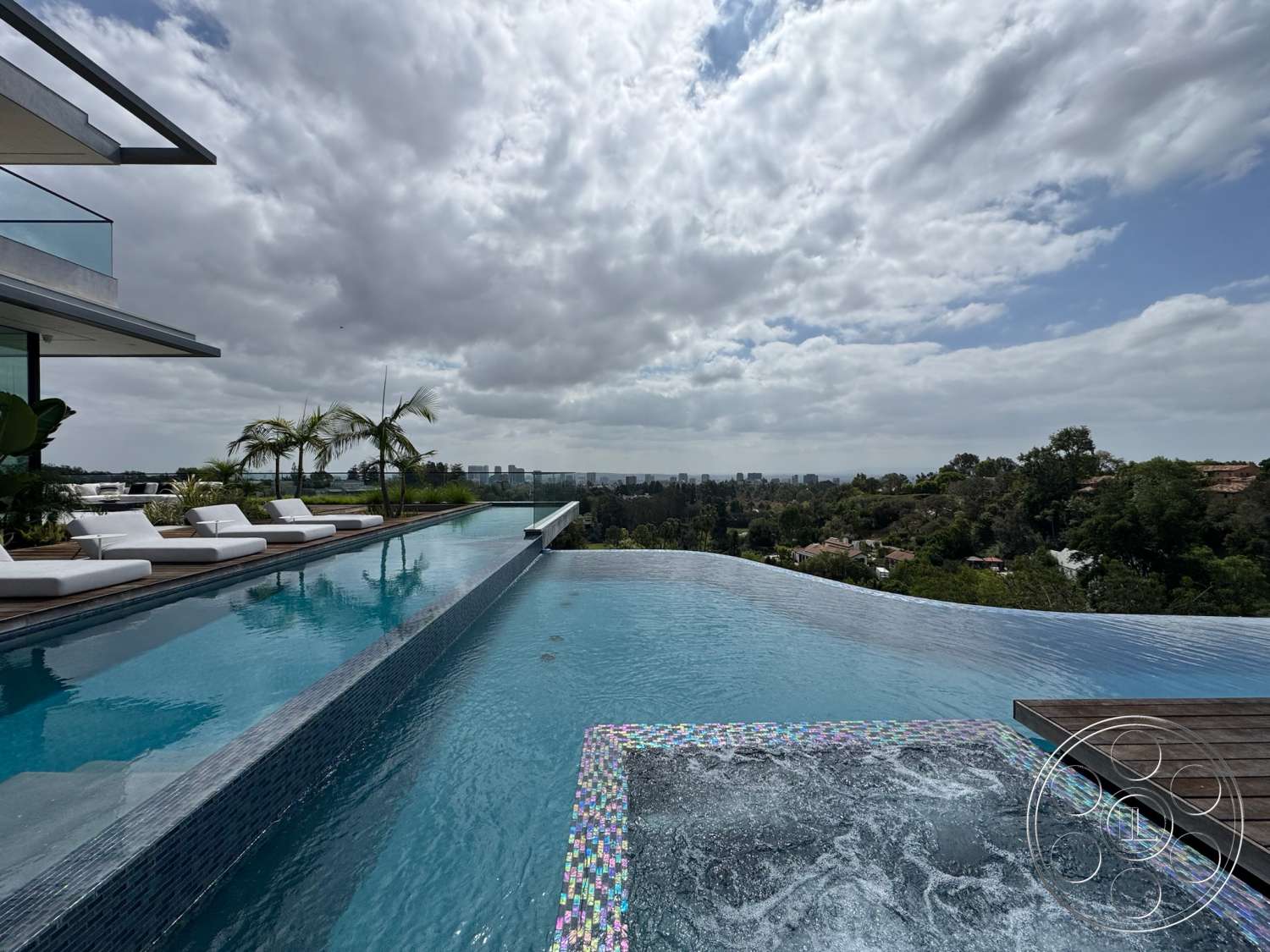 The Bellagio Estate - exterior, landscaped garden, modern architecture, glass railing, concrete patio, outdoor lounge area, city skyline view, infinity pool, cloudy sky, tile pool deck, wood poolside decking