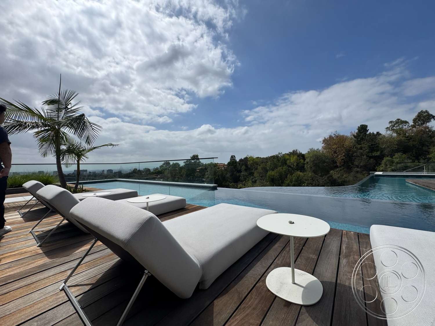 The Bellagio Estate - exterior, outdoor seating area, glass railing, mountain view, infinity pool, modern lounge chairs, wood deck flooring, concrete pool edge, landscaped garden with palm trees