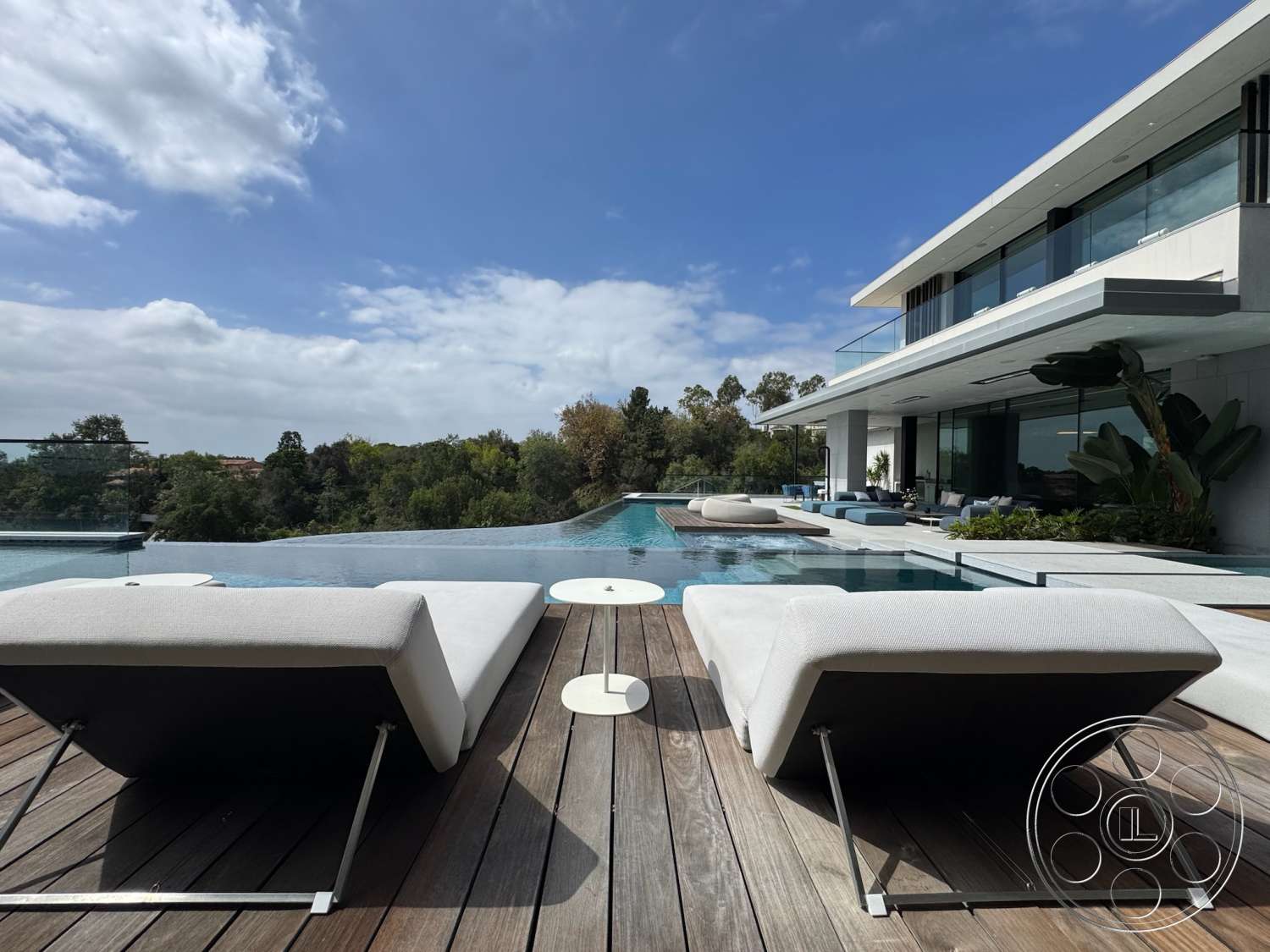 The Bellagio Estate - exterior, flat roof, outdoor seating area, glass railing, textured concrete walls, modern landscaping, open-air patio, infinity pool, large sliding glass doors, wood deck flooring, concrete pool border, minimalist architectural style, luxury lounge chairs, panoramic nature view