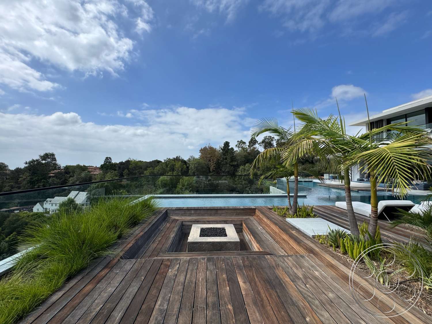The Bellagio Estate - exterior, contemporary design elements, modern architectural style, poolside lounge area, wood deck patio flooring, floor-to-ceiling glass panels, infinity pool with glass edge, built-in fire pit, slanted landscaping with ornamental grass, surrounding green hillside view