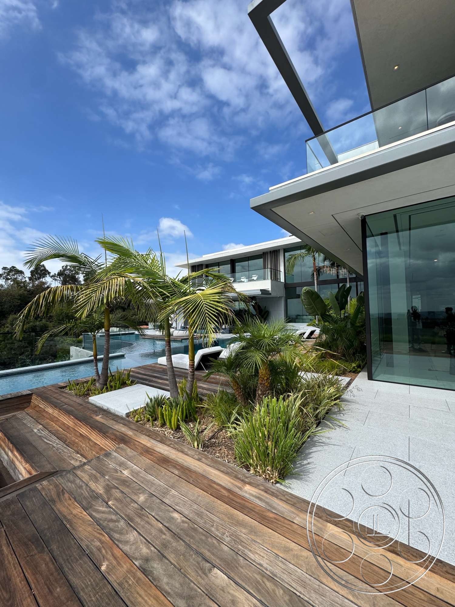 The Bellagio Estate - exterior, landscaped garden, flat roof, palm trees, open floor plan, glass sliding doors, concrete walls, floor-to-ceiling windows, modern architectural style, infinity pool, textured stone flooring, concrete pool deck, large overhang, wood deck patio