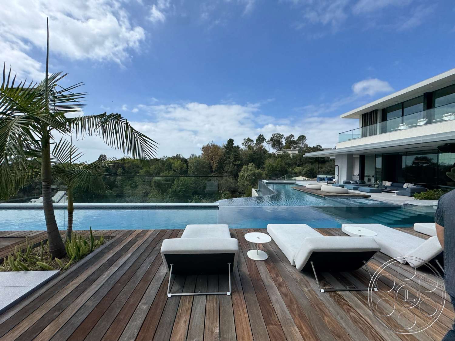The Bellagio Estate - exterior, glass sliding doors, glass railing, concrete patio, floor-to-ceiling windows, outdoor lounge area, modern architectural style, tropical landscaping, infinity pool, rectangular pool, landscaped garden area, wood deck flooring, sectional outdoor sofa