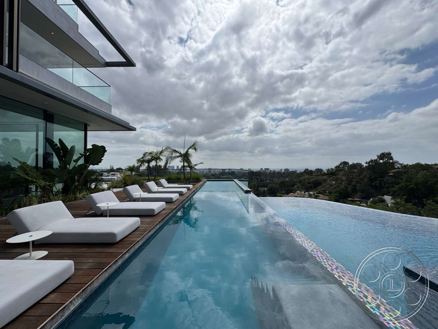 The Bellagio Estate - glass railing, wooden deck, modern architectural style, city skyline view, landscape plants, outdoor lounging area, open-air patio, infinity pool, concrete pool deck, luxury lounge chairs