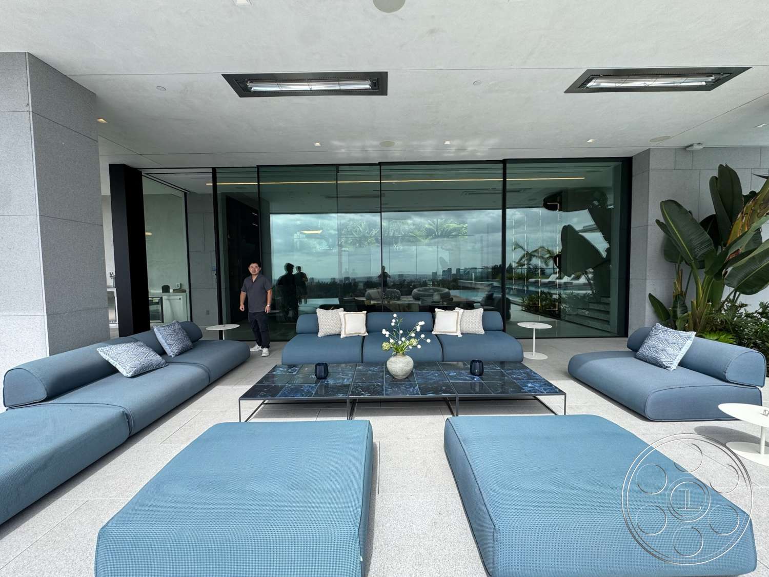The Bellagio Estate - exterior, glass sliding doors, marble coffee table, city skyline view, modern outdoor seating, concrete patio flooring, potted ornamental plants, indoor-outdoor living space, blue upholstered outdoor furniture