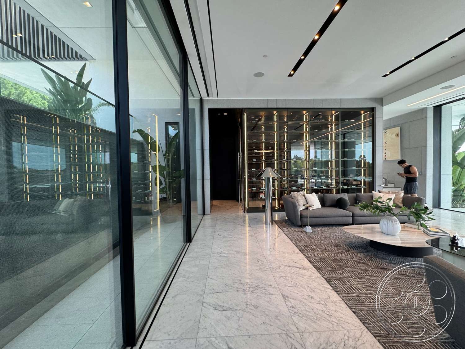 The Bellagio Estate - neutral color palette, indoor plants, open floor plan, dark cabinetry, floor-to-ceiling windows, marble flooring, luxury living room, plush area rug, black steel accents, sleek minimalist design, glass wall panels, modern wall lighting, built-in wine rack, contemporary sofa, structured ceiling details