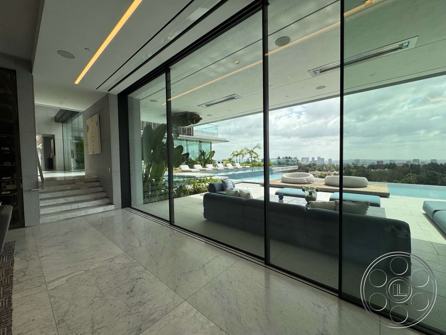 The Bellagio Estate - open floor plan, modern furniture, glass walls, contemporary architecture, city skyline view, marble flooring, luxury living room, outdoor terrace, landscape greenery, stone steps, linear recessed lighting, infinity pool view