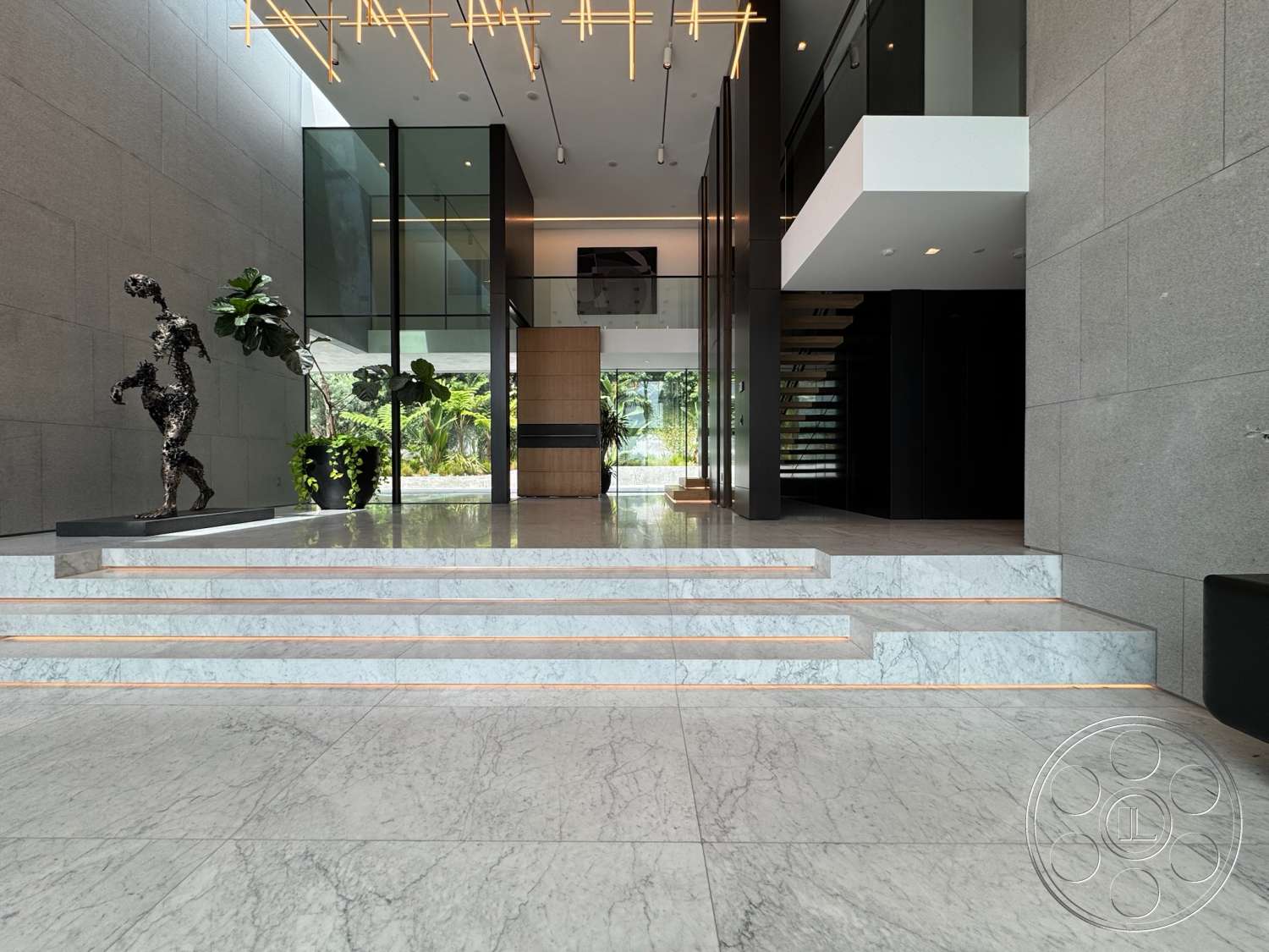 The Bellagio Estate - floor-to-ceiling windows, black metal railing, lush garden view, warm natural light, glass partition walls, indoor plant accents, gray stone wall panels, wooden feature wall, exposed ceiling lighting fixtures, contemporary art sculpture, modern staircase design, marble entrance flooring, marble steps with integrated lighting, open foyer design
