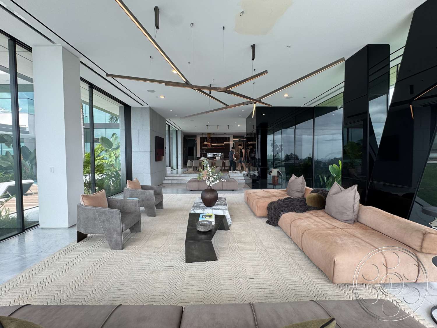 The Bellagio Estate - high ceilings, neutral color palette, kitchen view, minimalist design, natural lighting, textured area rug, open layout, sliding glass doors, planter with greenery, marble flooring, dark wood coffee table, architectural detailing, modern sectional sofa, exposed ceiling lights, glass wall panels, contemporary accent chairs