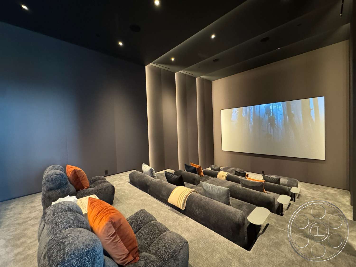 The Bellagio Estate - dim ambient lighting, large projection screen, modern ceiling design, soundproof wall treatments, neutral colored throw pillows, dark gray carpet flooring, theater room seating, reclining sofas, custom upholstered furniture, cosy movie atmosphere