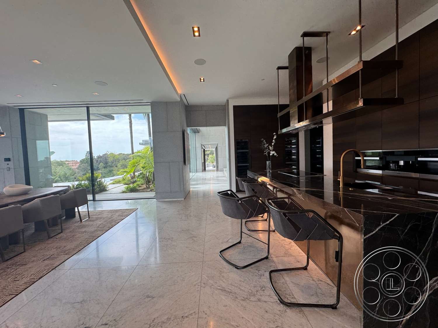 The Bellagio Estate - natural light, recessed lighting, textured area rug, glass sliding doors, seamless indoor-outdoor transition, floor-to-ceiling windows, minimalist cabinetry, open concept living space, polished marble flooring, modern dining area, contemporary kitchen design, black marble kitchen island, lush outdoor greenery view, black steel bar stools