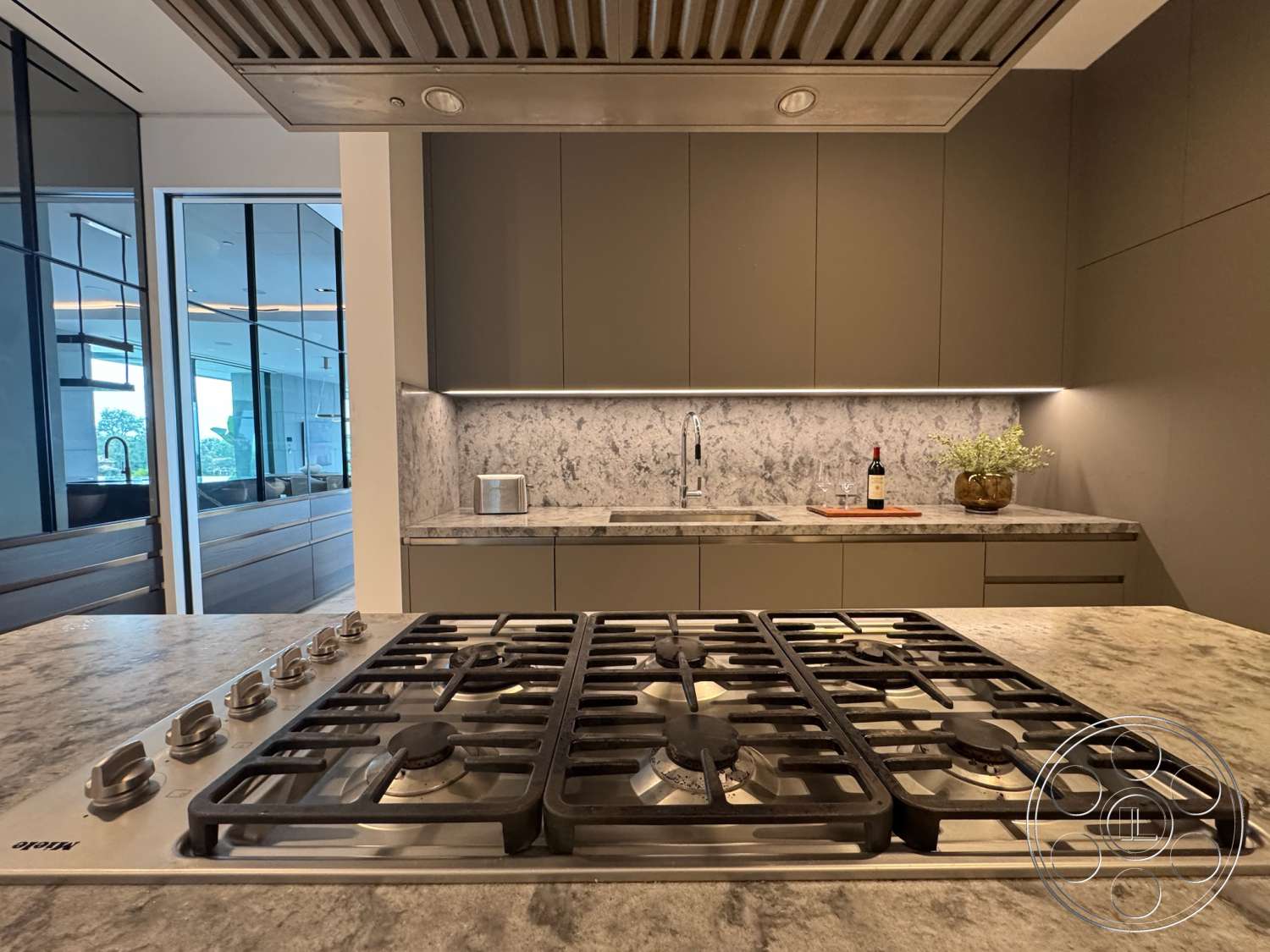 The Bellagio Estate - contemporary design, minimalist aesthetic, marble backsplash, open kitchen layout, stainless steel gas cooktop, quartz countertop with integrated gas cooktop, dark cabinetry with sleek finish, undermount sink with modern faucet, LED lighting under upper cabinets, glass door to adjacent rooms