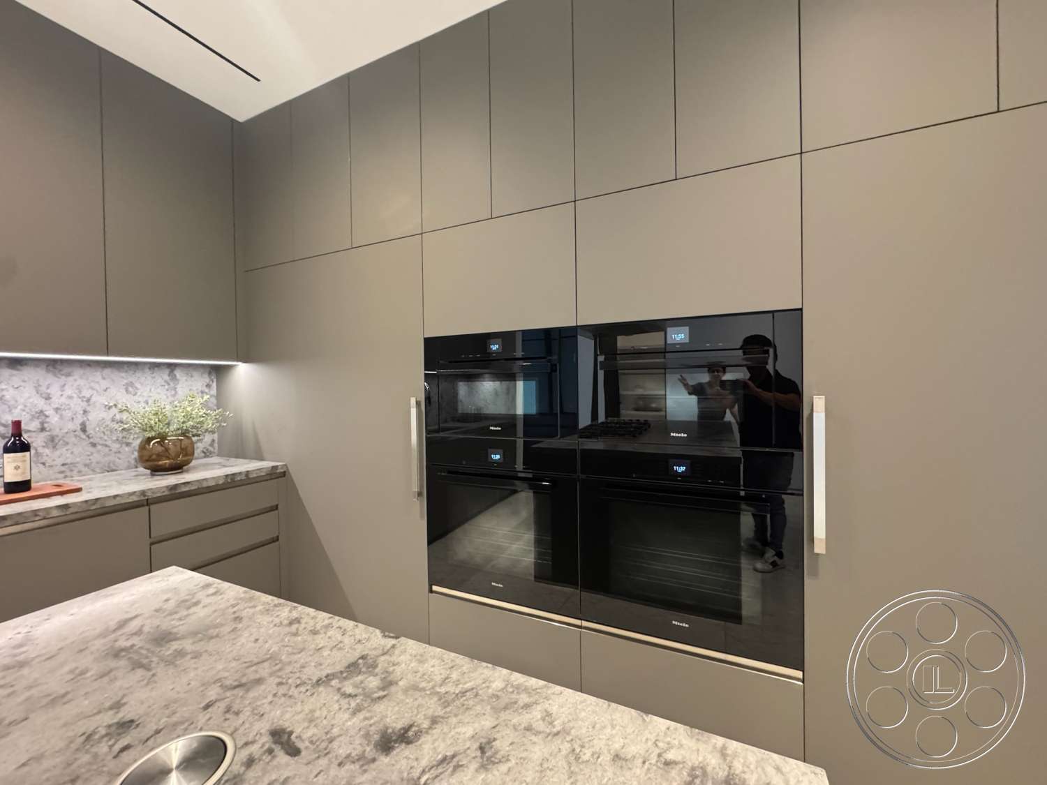 The Bellagio Estate - under-cabinet lighting, textured stone surface, minimalist kitchen design, marble kitchen backsplash, concrete kitchen countertops, gray flat-panel cabinets, black built-in oven, black cooktop