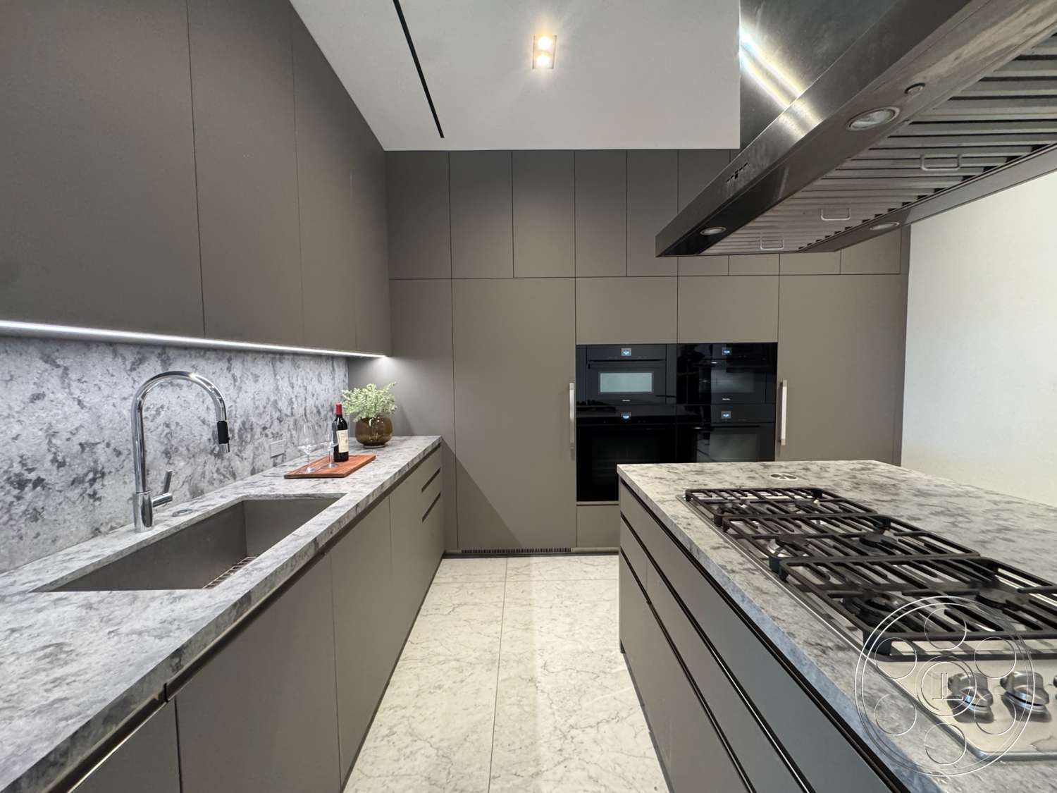 The Bellagio Estate - stainless steel appliances, marble countertop, stone backsplash, grey cabinetry, modern kitchen design, interior kitchen, minimalist kitchen decor, linear ceiling lights, black oven units, slab marble flooring