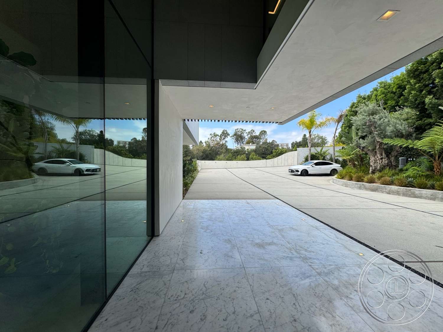 The Bellagio Estate - exterior, modern architectural style, concrete driveway, curved driveway, marble flooring, floor-to-ceiling glass walls, landscaped garden with tropical plants, flat roof with overhang, reflective glass panels