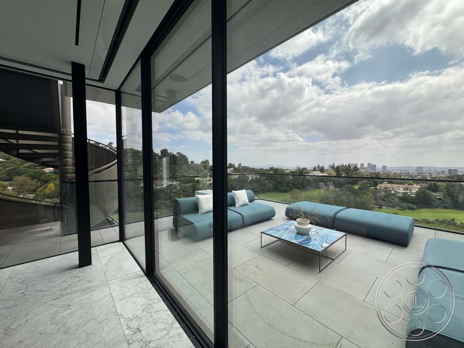 The Bellagio Estate - exterior, glass sliding doors, metal coffee table, mountain view setting, modern architectural details, rectangular outdoor seating area, marble patio flooring, sloped hillside, contemporary glass railings, textured blue outdoor cushions, open terrace layout
