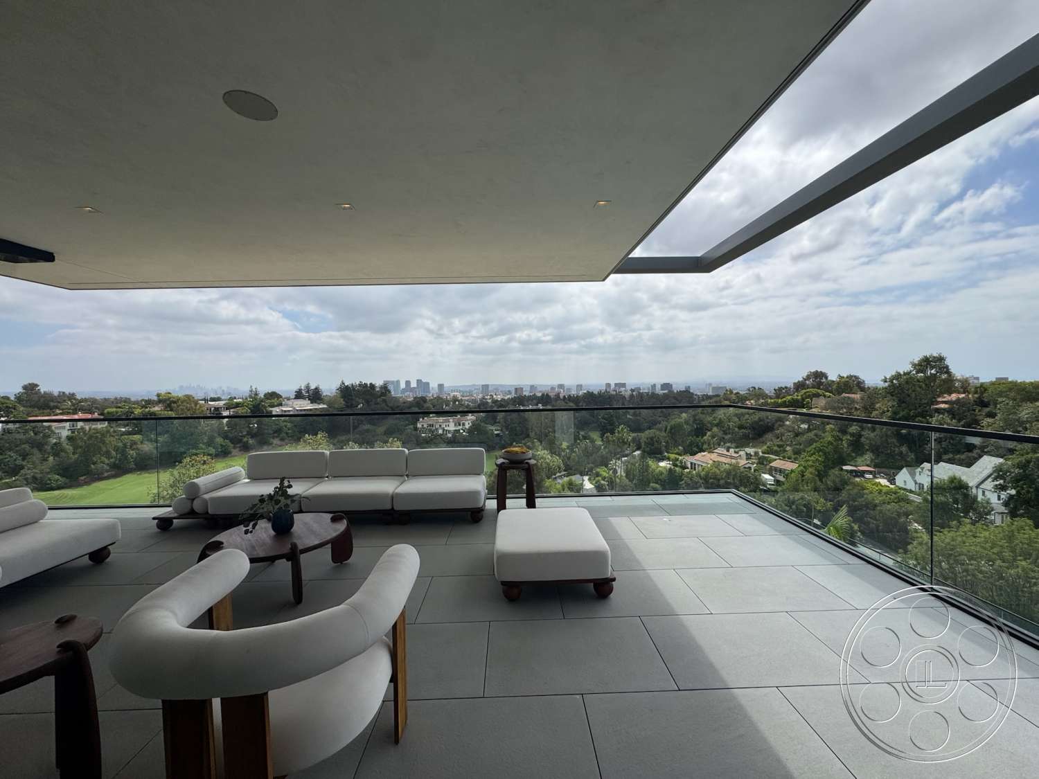 The Bellagio Estate - exterior, minimalist design elements, city skyline view, large sliding glass doors, modern outdoor seating, concrete patio flooring, flat roof overhang, glass railing balcony, lush green landscape view, rectangular outdoor coffee table, luxury apartment balcony