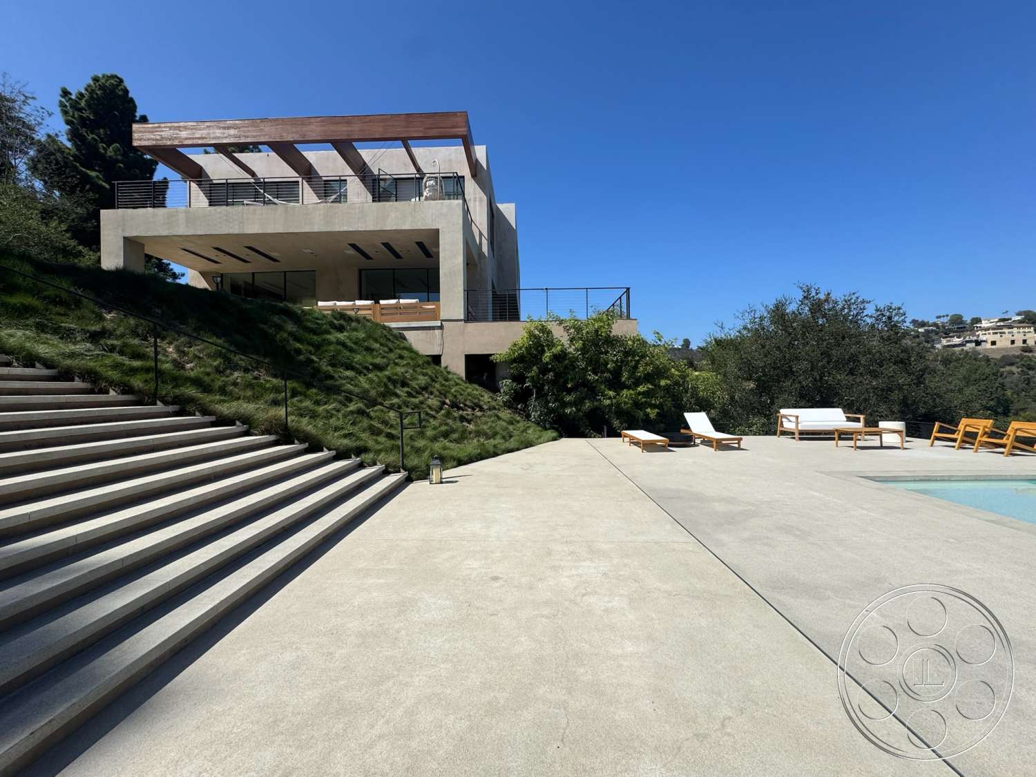Modern 527 - exterior, modern architecture, glass sliding doors, landscaped hillside, concrete patio flooring, concrete exterior walls, lush greenery surrounding, minimalist outdoor furniture, sunny outdoor environment, open terrace with railing, staircase with concrete steps, city view setting, flat roof with wooden overhang, expansive swimming pool area, horizontal wood slat detailing
