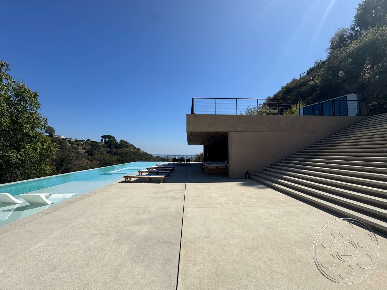 Modern 527 - exterior, minimalist design, landscaped greenery, steel railing, modern architectural style, infinity pool, wooden lounge chairs, large overhang, concrete patio floor, sloped hillside setting