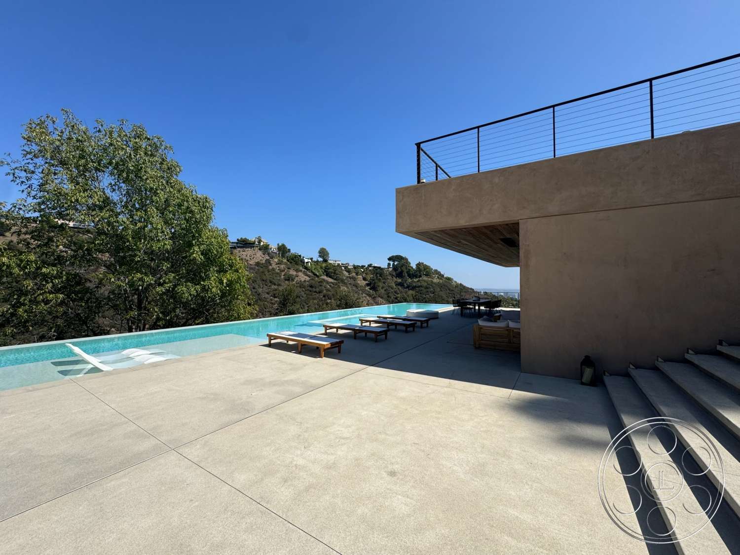 Modern 527 - exterior, outdoor seating area, landscape view, modern architectural style, infinity pool, wooden lounge chairs, concrete patio flooring, metal balcony railing, elevated outdoor terrace, plastered concrete walls