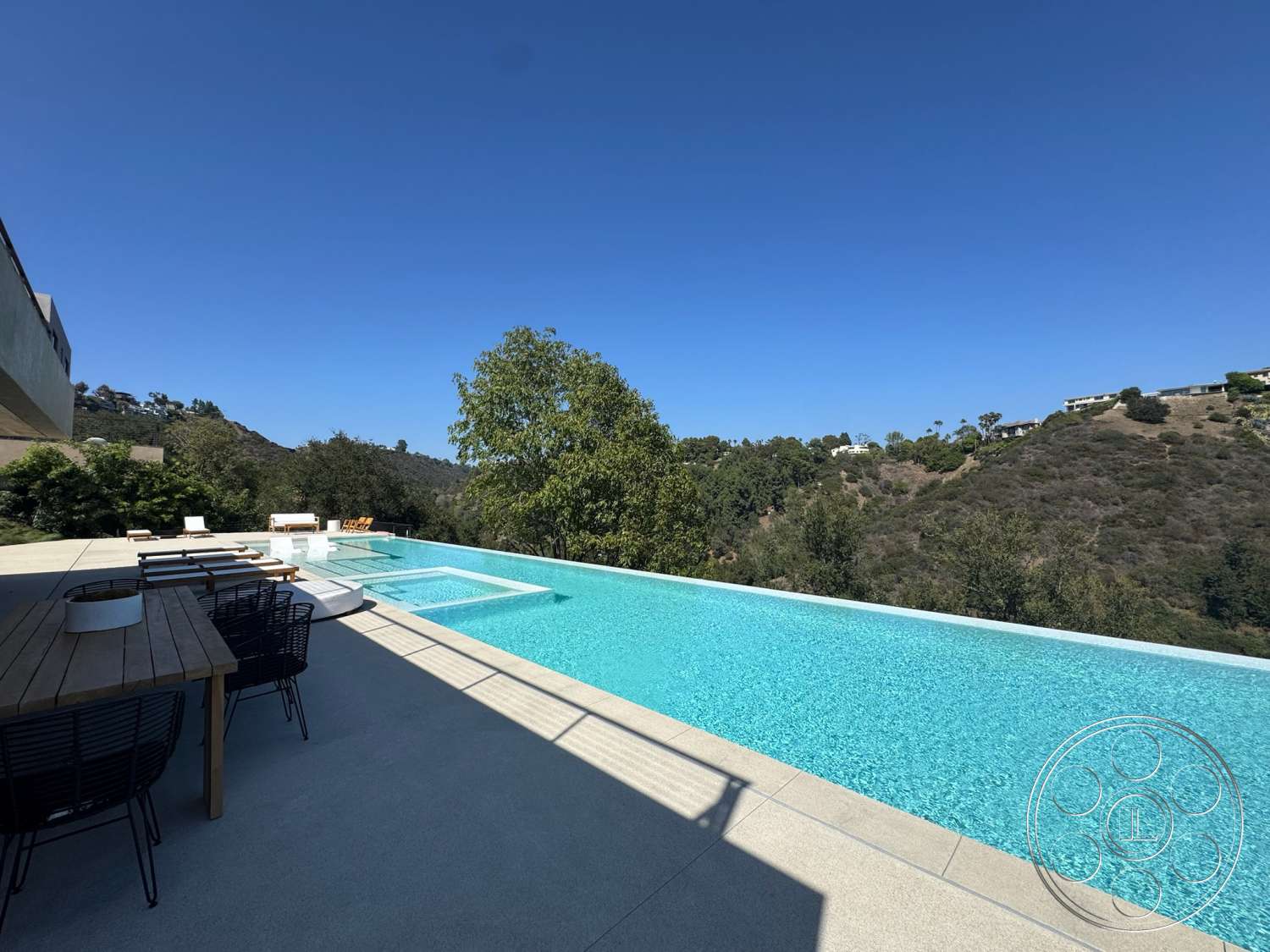 Modern 527 - exterior, wood dining table, outdoor seating area, rectangular swimming pool, contemporary architecture, clear blue sky, infinity pool, concrete patio flooring, black metal dining chairs, landscaped hillside setting