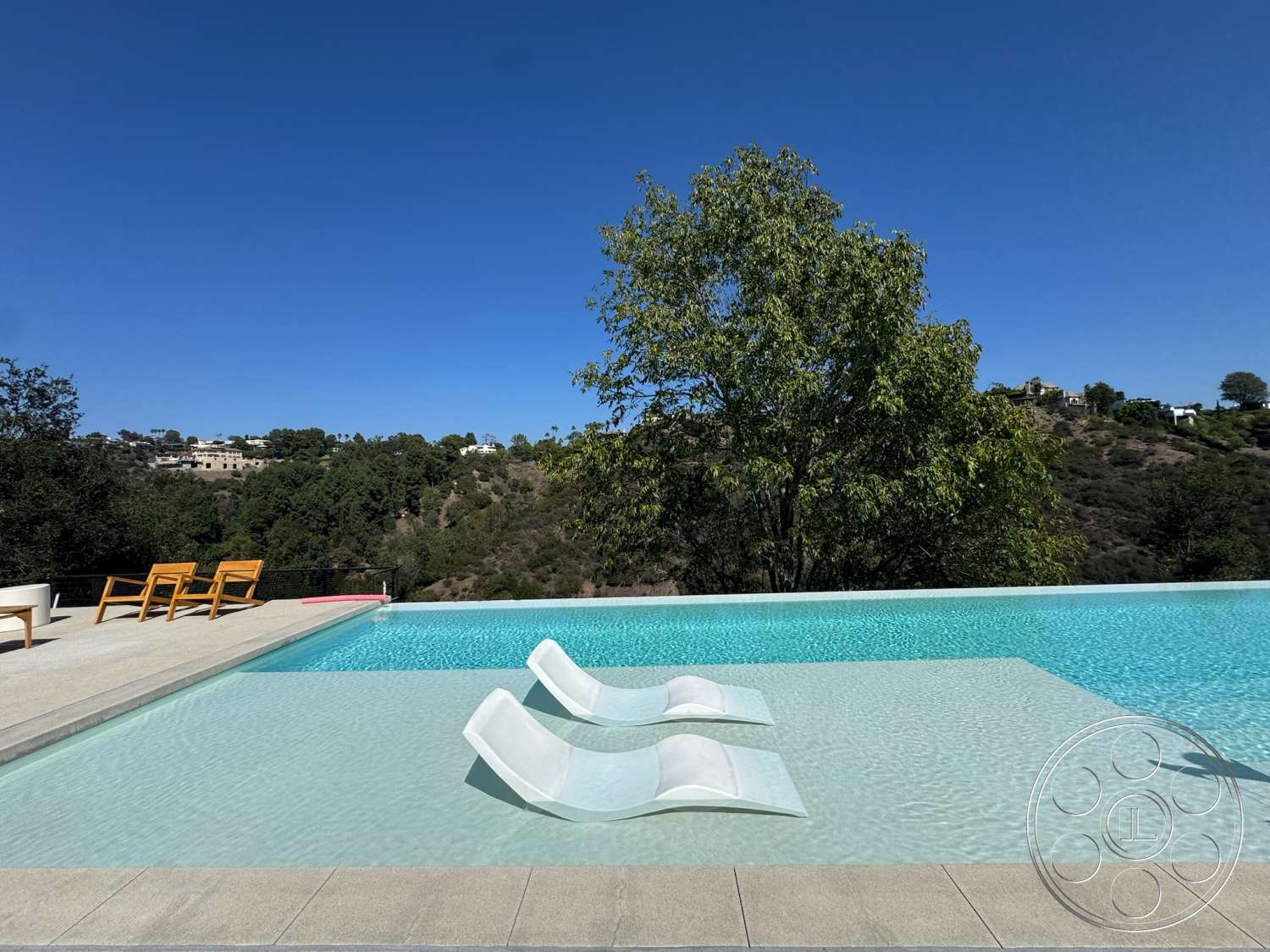 Modern 527 - exterior, surrounding trees, modern architectural style, landscaped hillside, blue sky, infinity pool, concrete pool border, concrete patio floor, clear glass pool edge, wooden chaise lounge chairs
