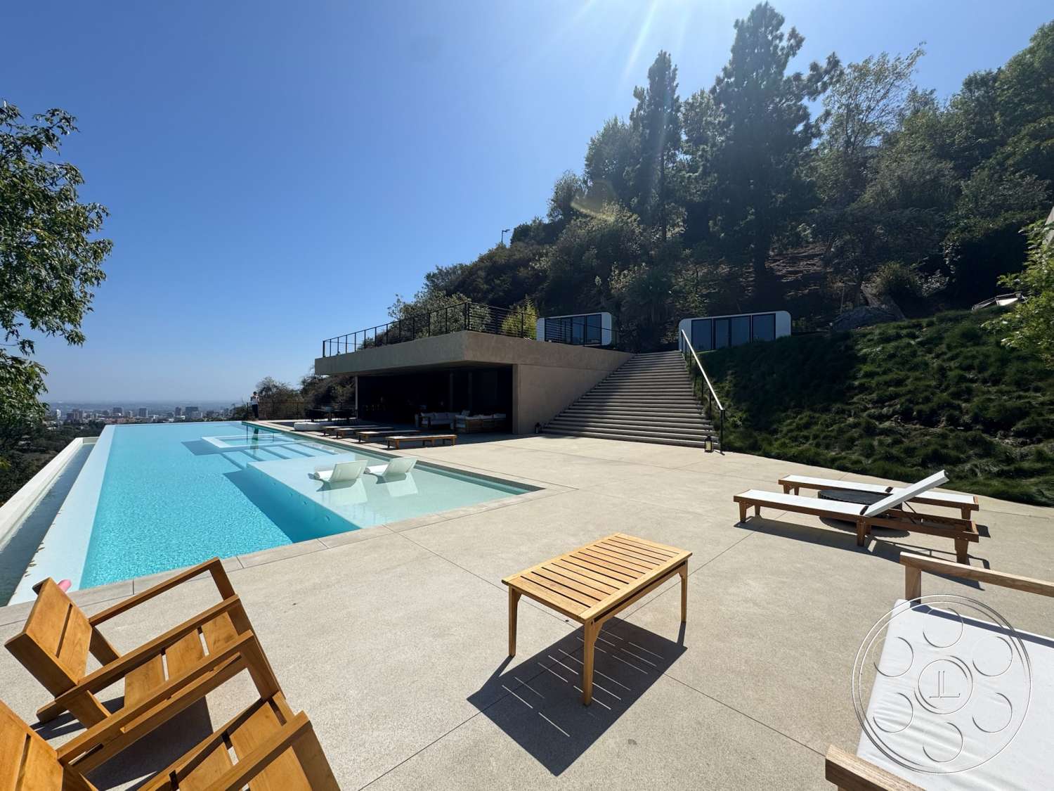 Modern 527 - exterior, modern architecture, minimalist design, glass railing, concrete stairs, open outdoor space, city skyline view, infinity pool, sloping green lawn, concrete pool patio, wood lounge chairs, landscaped hill backdrop