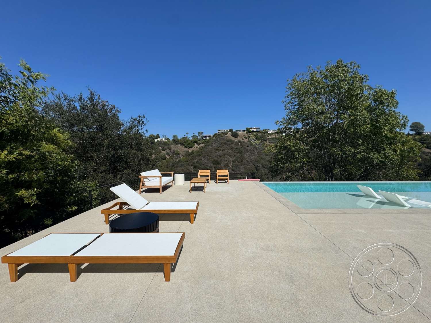 Modern 527 - concrete pool deck, natural greenery backdrop, clear blue sky view, rectangular infinity pool, landscaped hillside setting, urban outdoor lounge area, hardwood lounge chairs, slate table