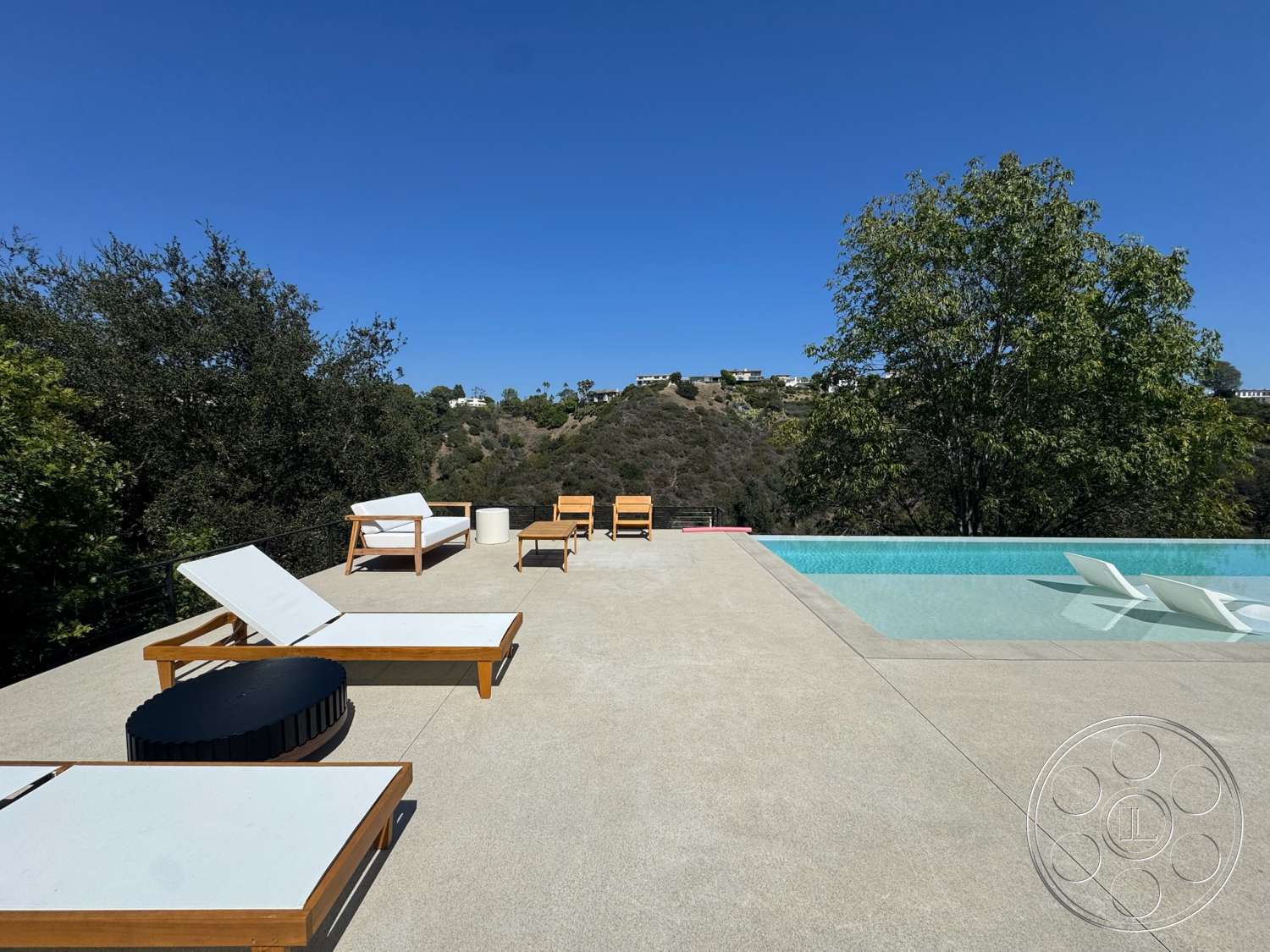 Modern 527 - exterior, rectangular swimming pool, clear blue sky, modern minimalist design, concrete patio surface, wooden deck chairs, wood lounge chairs, black cylindrical outdoor table, green hillside view