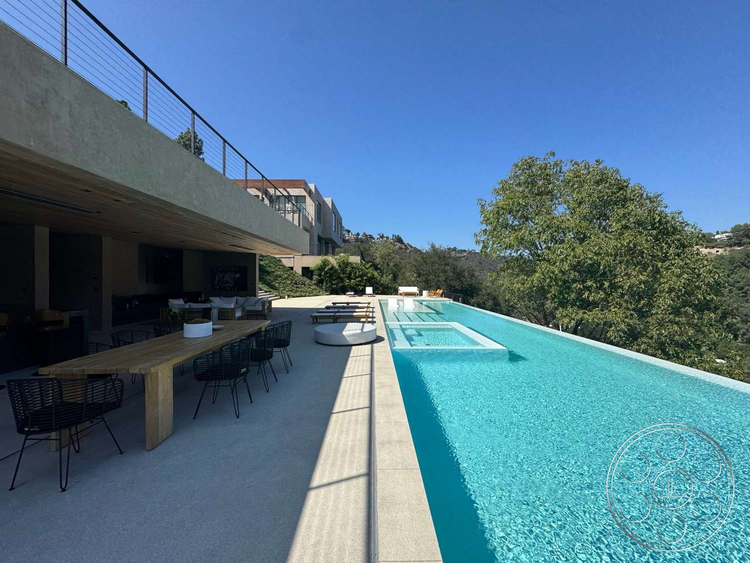 Modern 527 - exterior, wood dining table, glass railing, landscaped hillside, clear blue sky, infinity pool, rectangular pool, exposed wood ceiling, stone terrace flooring, black metal outdoor chairs, concrete pool decking, modern outdoor lounge seating