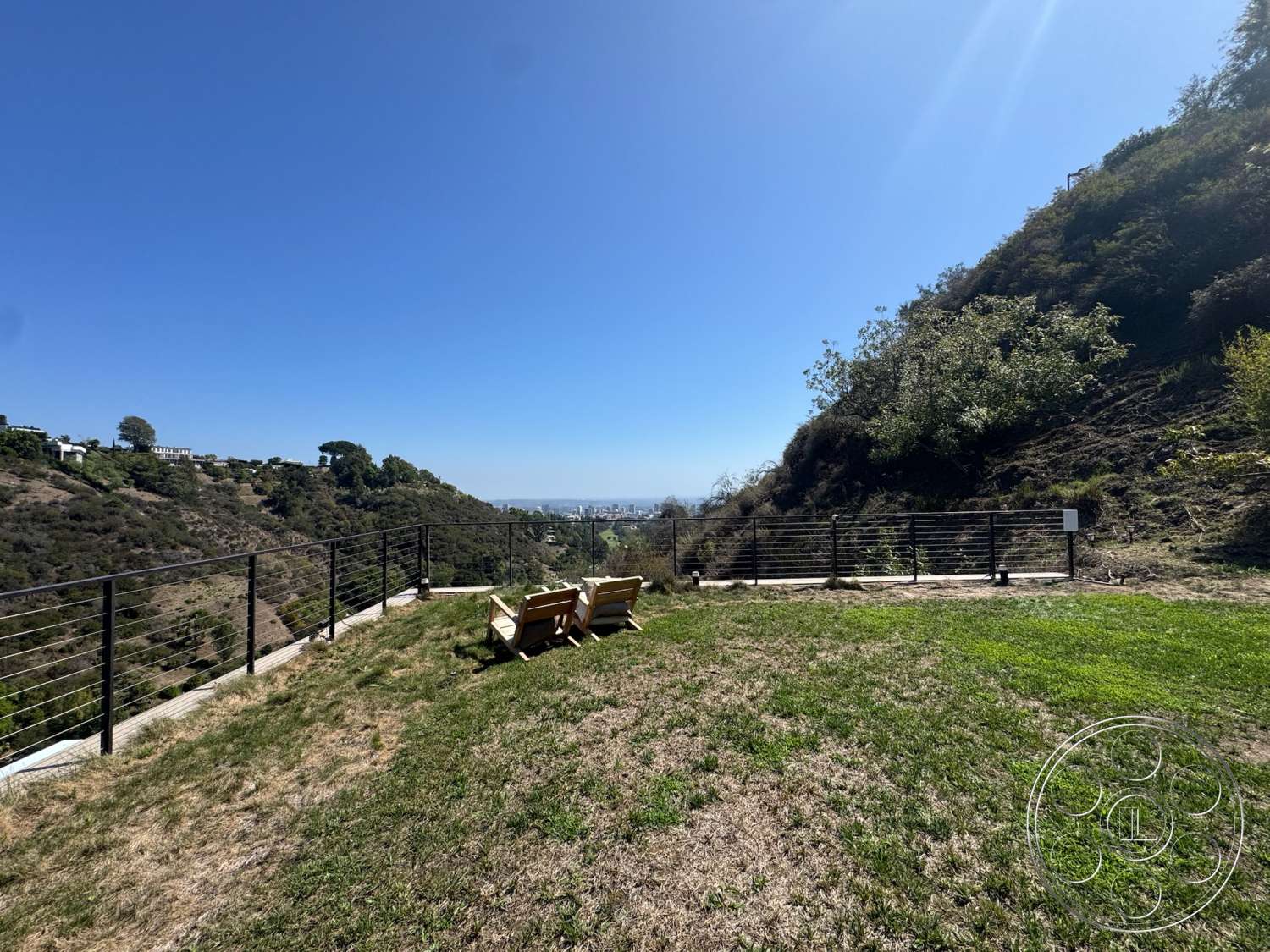 Modern 527 - exterior, city skyline view, clear blue sky, wooden lounge chairs, natural terrain, dense greenery, metal railing fencing, grassy hillside landscape, slope topography