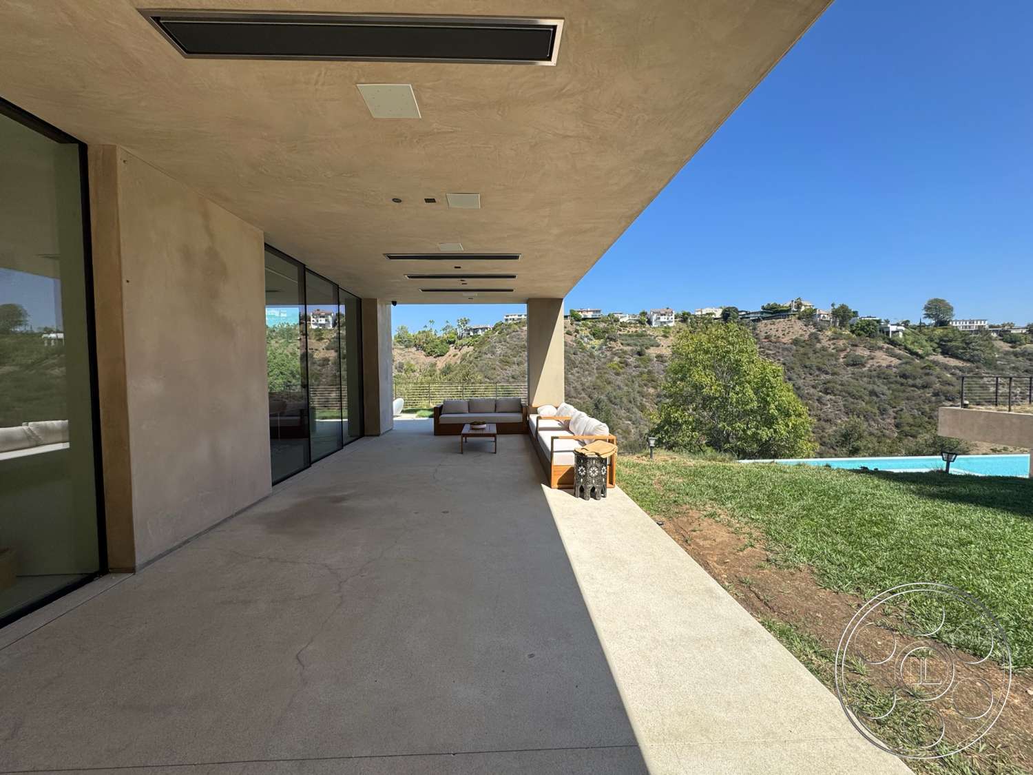Modern 527 - exterior, flat roof, minimalist design, sliding glass doors, panoramic views, stucco walls, large overhang, concrete patio flooring, indoor-outdoor living space, natural grass area, furnished outdoor lounge area, landscaped hillside background