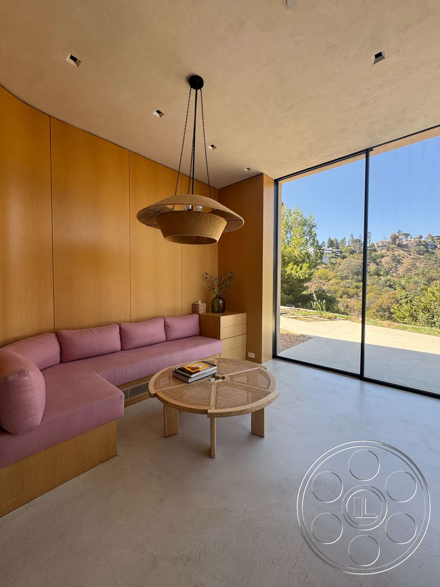 Modern 527 - neutral color palette, minimalist design, concrete flooring, glass sliding doors, wood accent wall, natural light from large windows, woven pendant light fixture, plaster ceiling, pink upholstered sectional sofa, modern coffee table with rattan elements